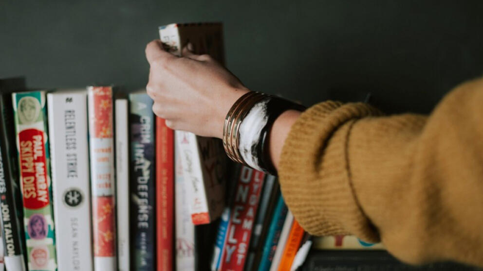 Девушка берет книгу с полки