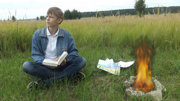 Мальчик читает книгу у костра
