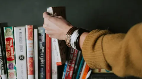 Девушка берет книгу с полки
